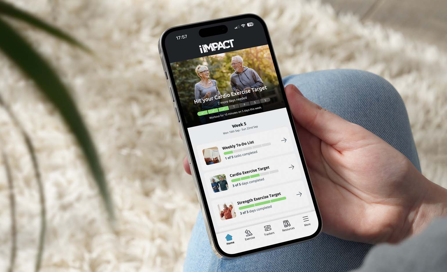 A person holding a mobile phone with the Home screen of i-IMPACT visible
